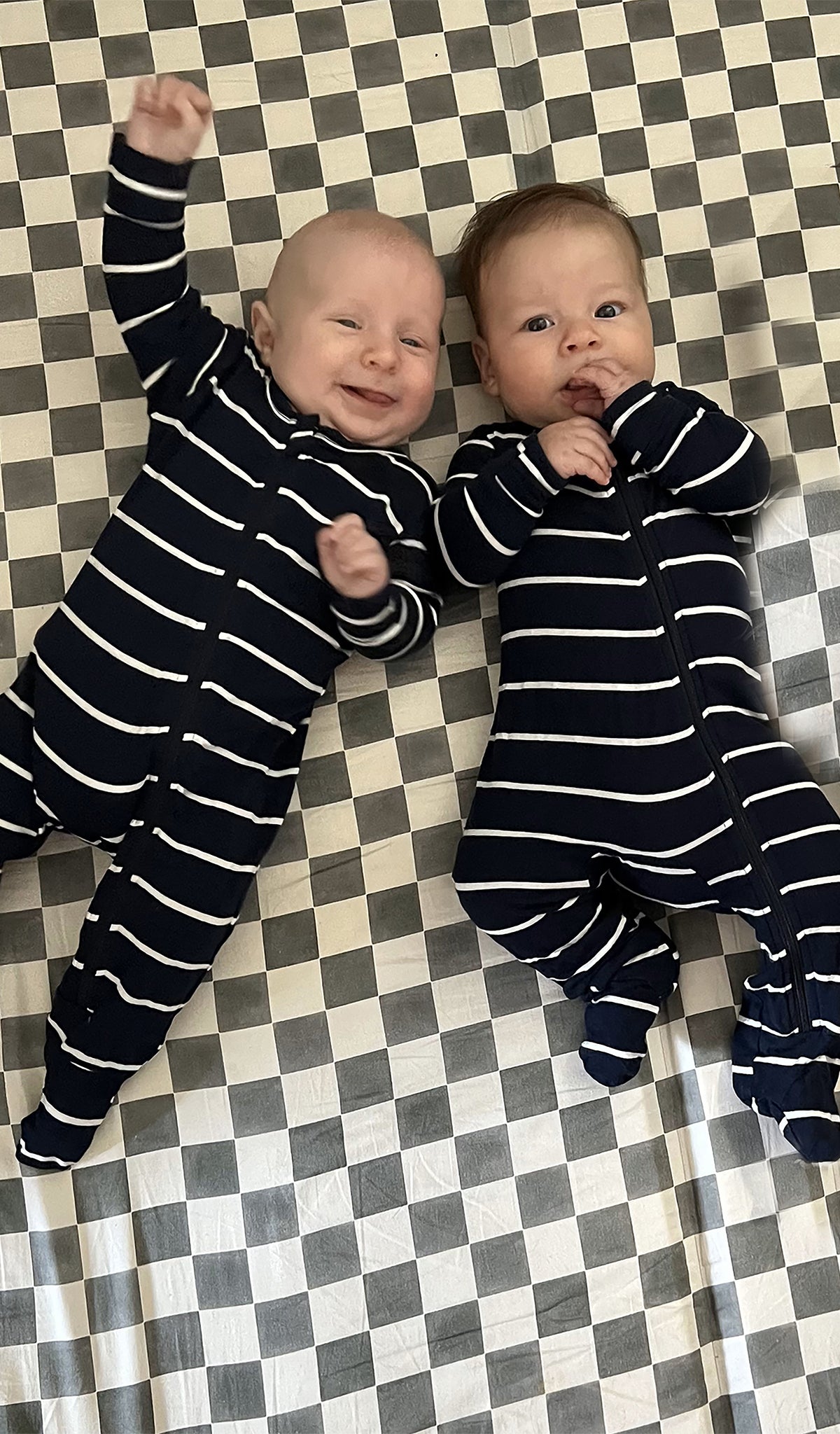 Navy Stripe Footie worn by two baby boys laying on a checkered blanket.