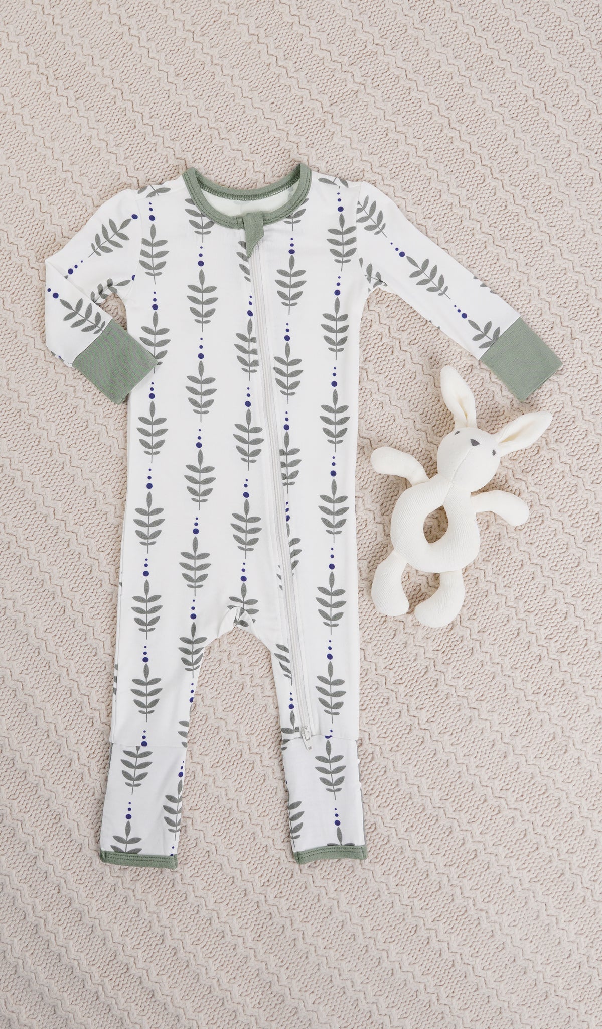 Eucalyptus Convertible Romper with long sleeves and zip front on knitted beige blanket with bunny rattle.