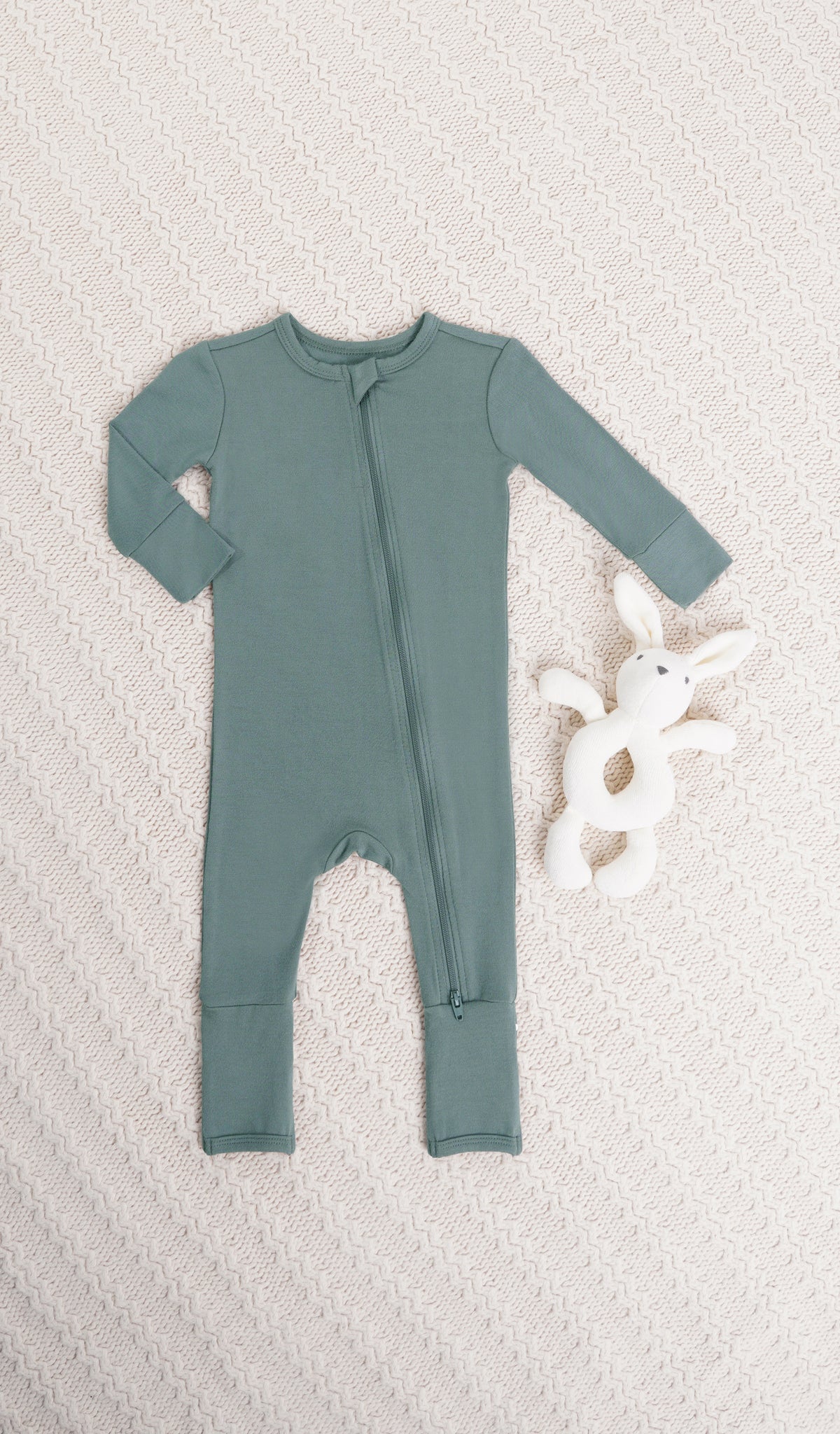 Fog Convertible Romper with long sleeves and zip front on knitted beige blanket with bunny rattle.