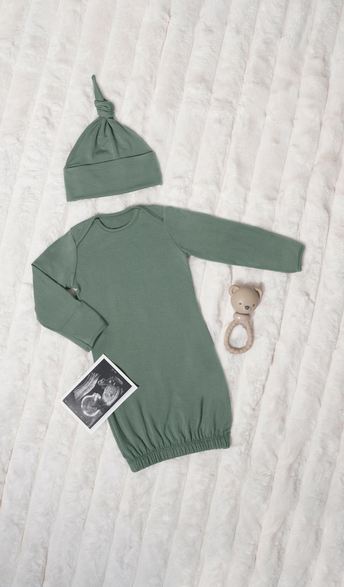 Basil Analise 5-Piece Set, gown and knotted hat for baby with rattle and ulstr sound image on a textured beige blanket.