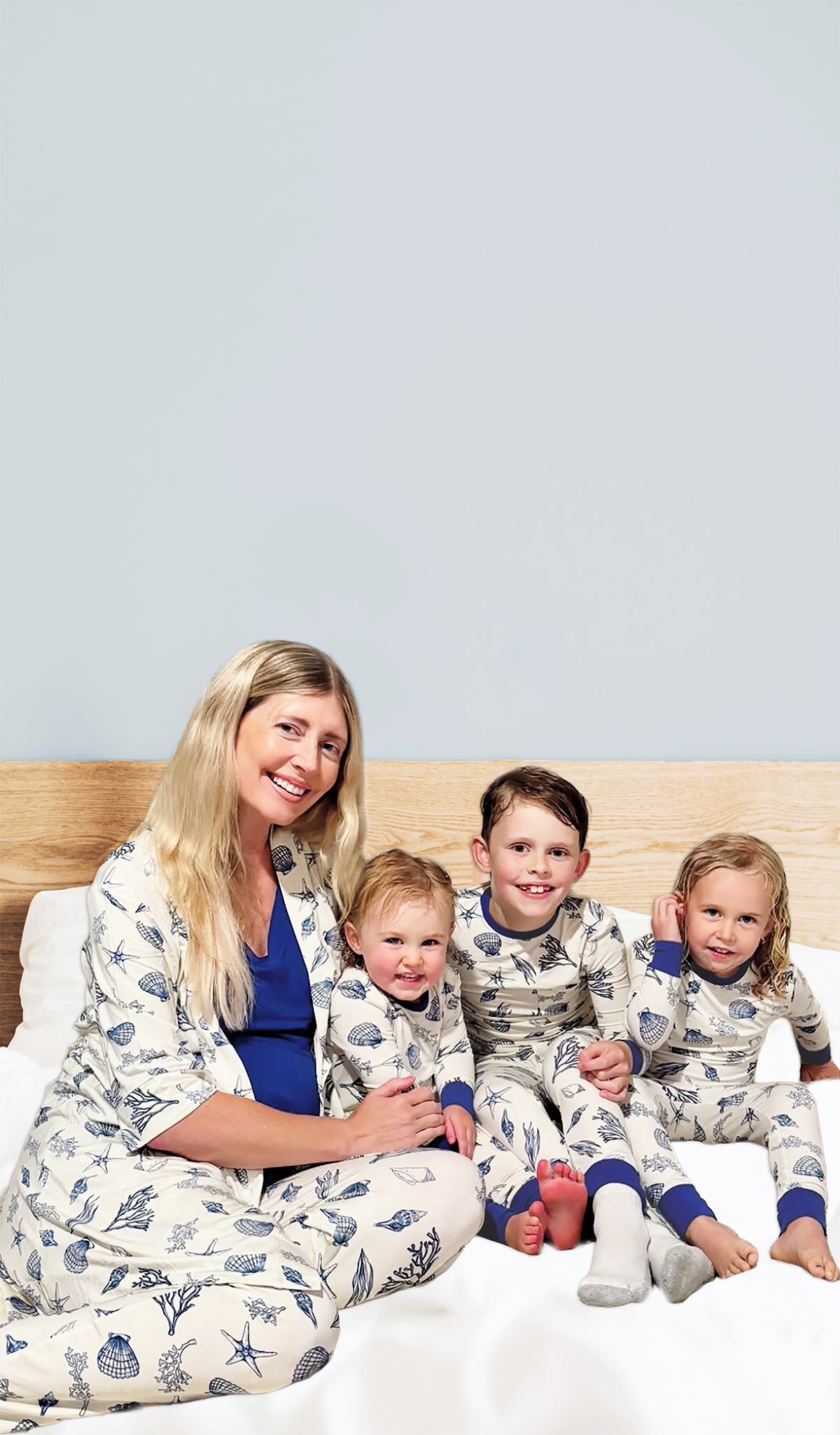 Woman and three children in matching Coastal print pajamas sitting on a bed.