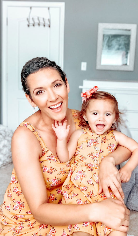 Mustard Floral Catalina Kids Dress. Woman wearing Savannah dress and holding little girl on lap who is wearing matching Catalina Kids Dress.