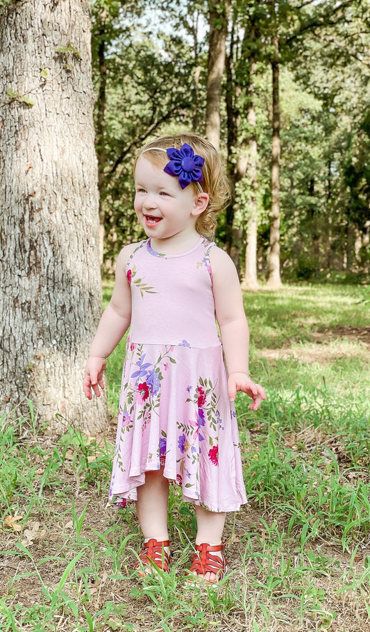 Dusty Rose Lucia Kids Twirly Dress. Little girl outside next to tree wearing Dusty Rose Lucia dress with purple flower headband.