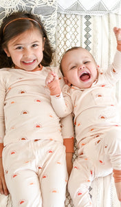 Little girl and baby boy wearing Sunrise Emerson pajamas while smiling.