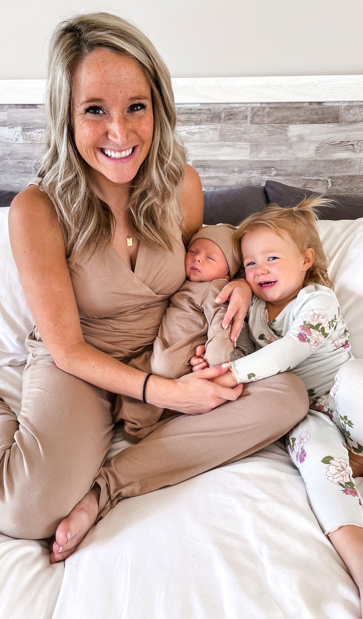 Latte Gown 2-Piece with long sleeve baby gown and matching knotted hat worn by sleeping baby while being hugged by his mom and sister..