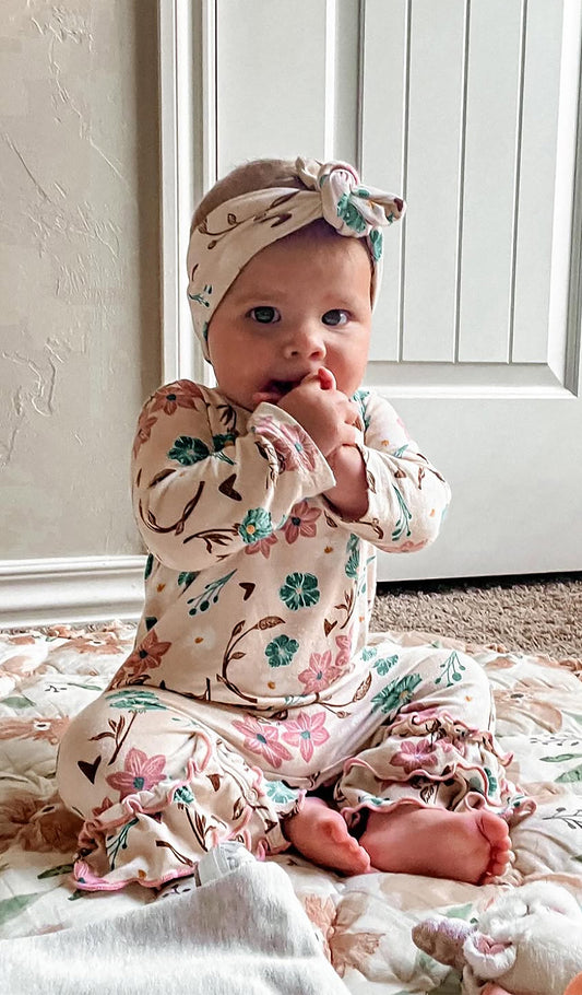 Magnolia Ruffle Romper and matching headwrap worn by baby girl sitting on a blanket.  