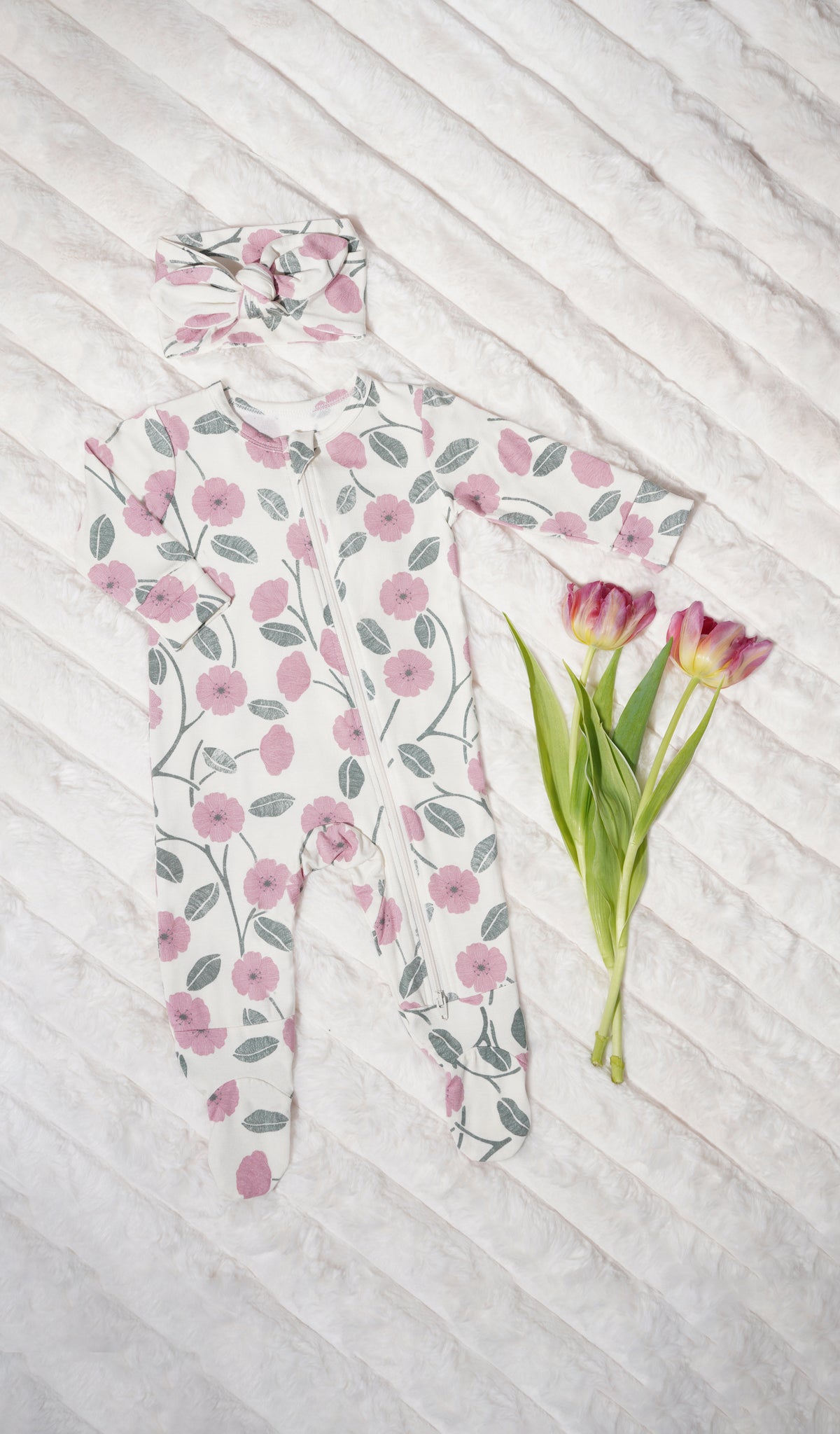 Honey Bloom Footie 2-Piece Set. Zip front footie for baby with matching headwrap and flowers on soft beige blanket.