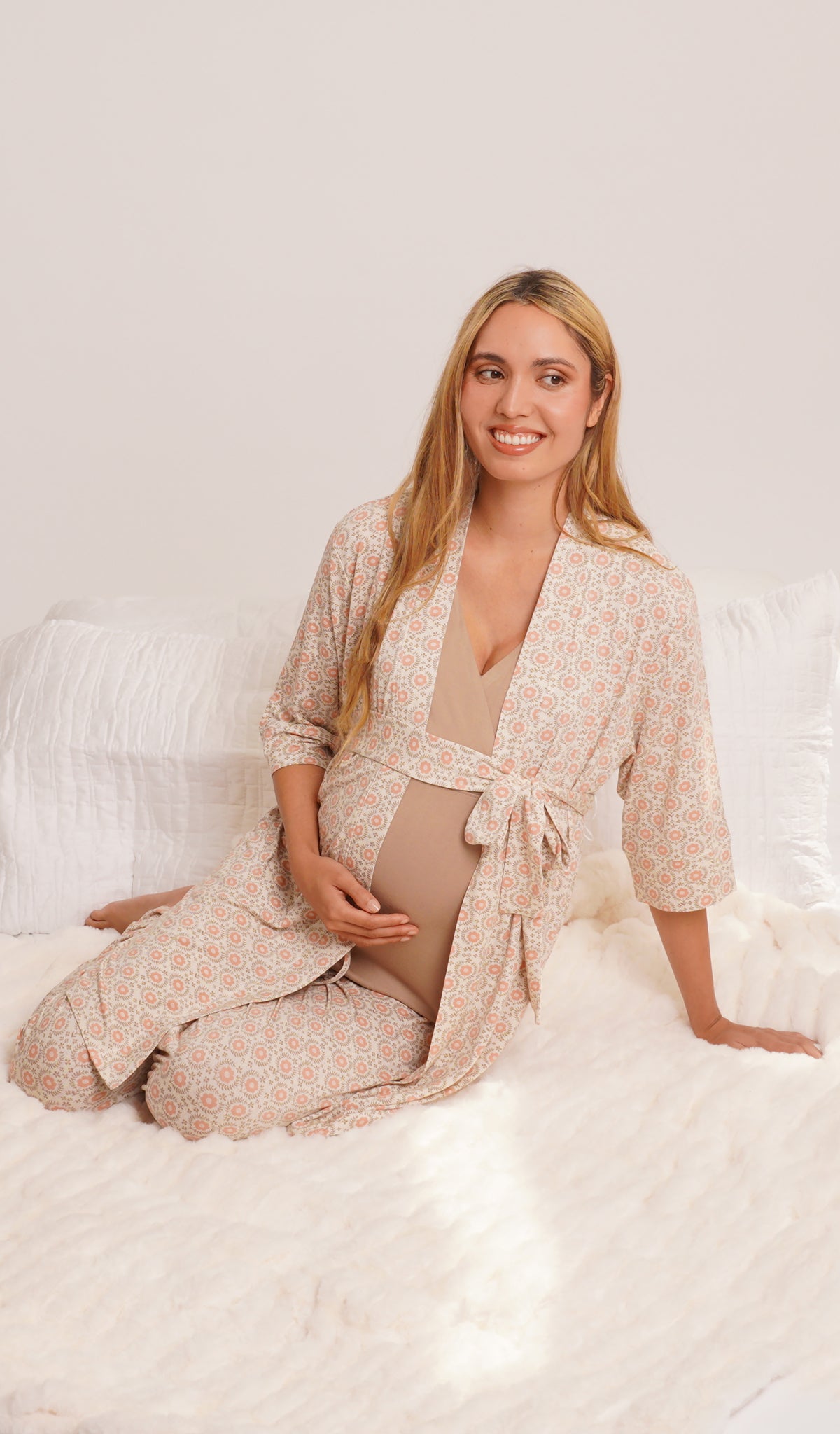 Bohemian Analise 5-Piece Set, woman wearing robe, tank top and pant sitting on bed leaning on one hand while holding belly with other hand.