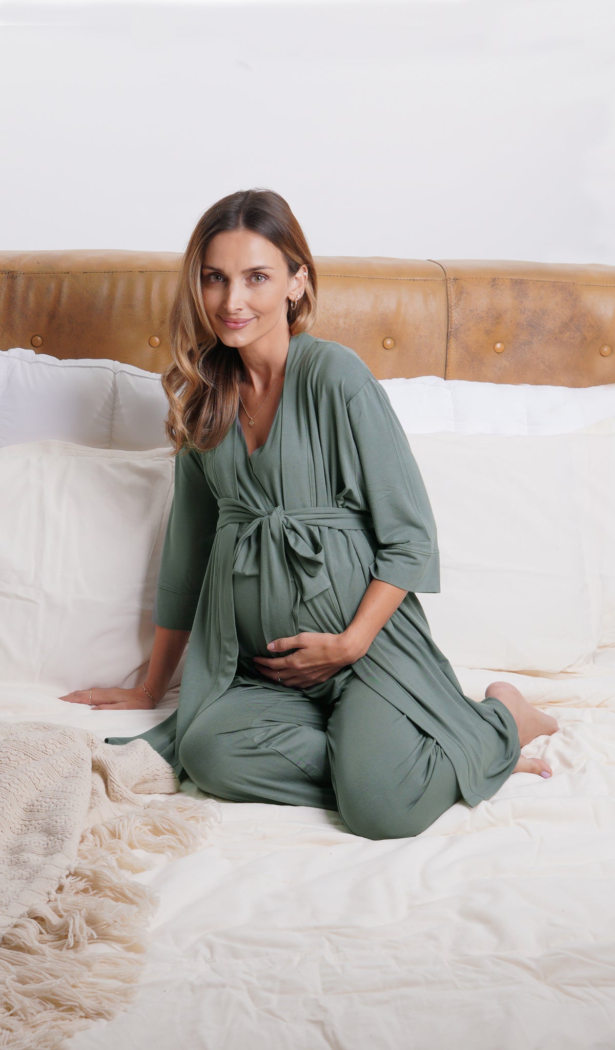 Fog Analise 5-Piece Set, woman wearing robe, tank top and pant sitting on bed leaning back on one hand while holding belly with other hand.