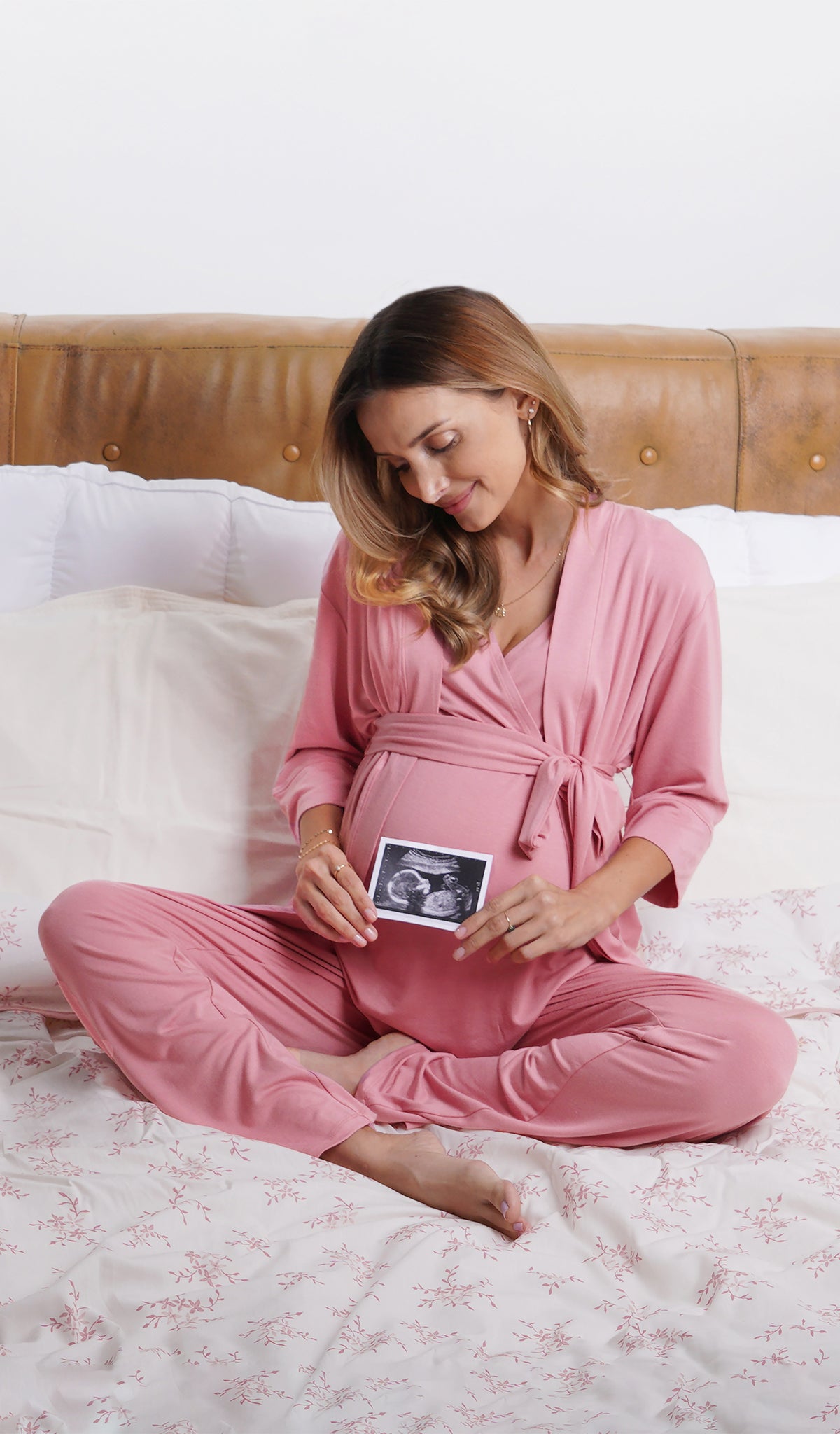 Rose Analise 5-Piece Set, woman wearing robe, tank top and pant sitting cross legged on a bed and holding an ultrasound in front of her belly.