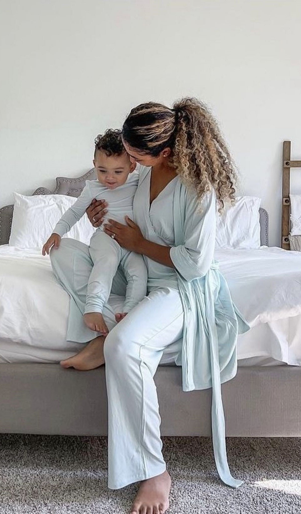 Whispering Blue Analise 5-Piece Set. Woman wearing 3/4 sleeve robe, tank top and pant while holding a baby wearing Emerson 2-piece top and pant PJ.