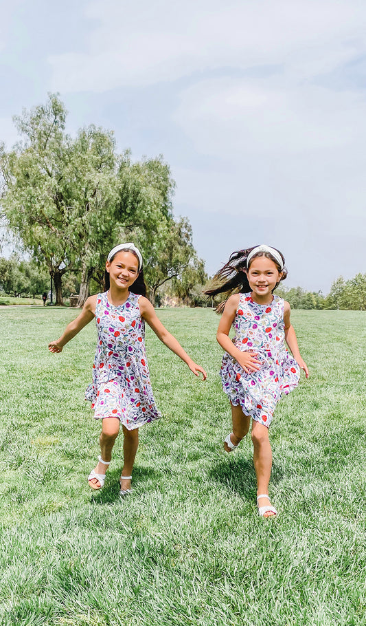 Lucia Kids Twirly Dress in Zinnia worn by two sisters running on a grass field.