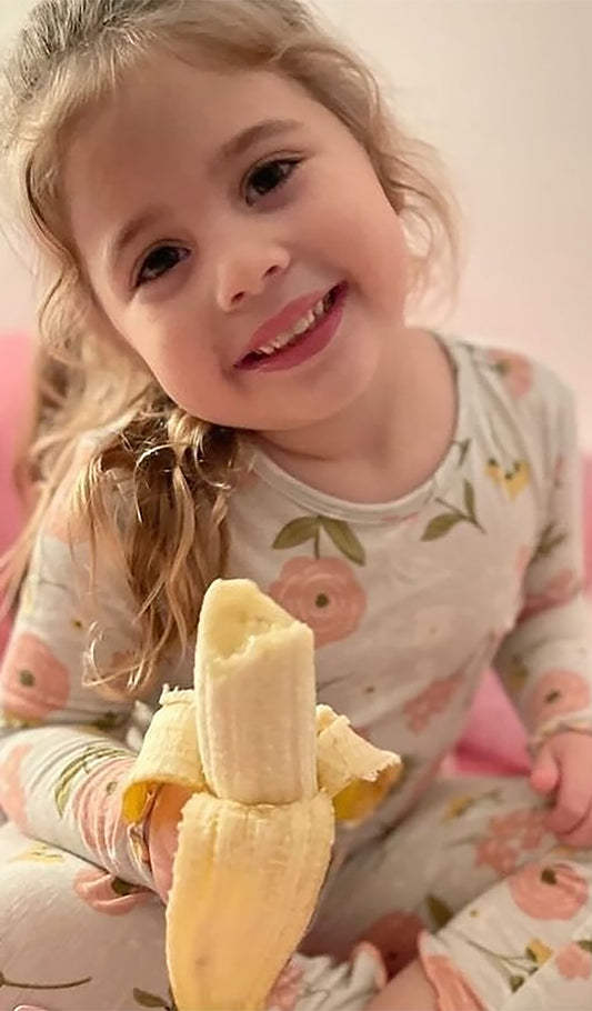 Carnation Charlie Kids 3-Piece Pant PJ worn by little girl eating a banana.  Headwrap not shown.