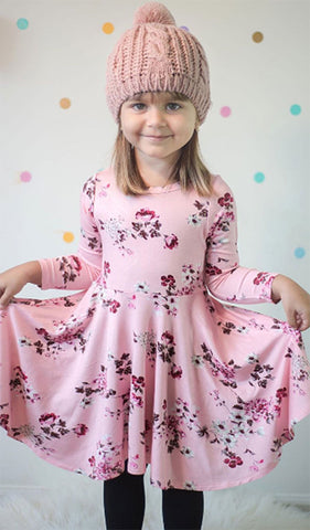 Blossom Kendyl Kids Twirly Dress. Little girl holding her skirt, wearing Kendyl long sleeve dress with twirly skirt and a pink beanie.