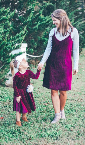 Merlot Kendyl Kids Twirly Dress. Little girl wearing Kendyl long sleeve dress and removeable flower pin on waist, holding hands with woman wearing matching Aurora Merlot dress.
