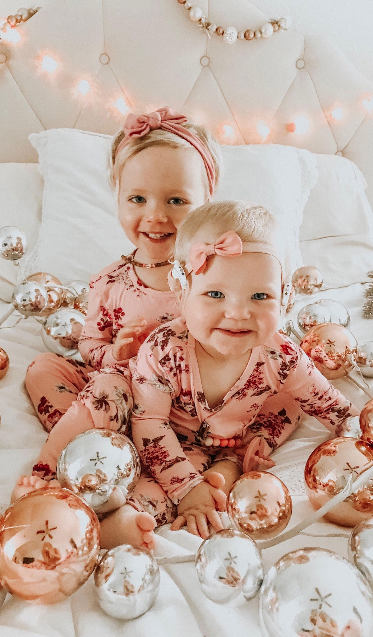 Blossom Charlie Baby 3-Piece Pant PJ. Little girl and baby sister sitting on bed with Christmas ball decoration garland wearing Charlie long sleeve top and pant from 3-Piece PJ set.