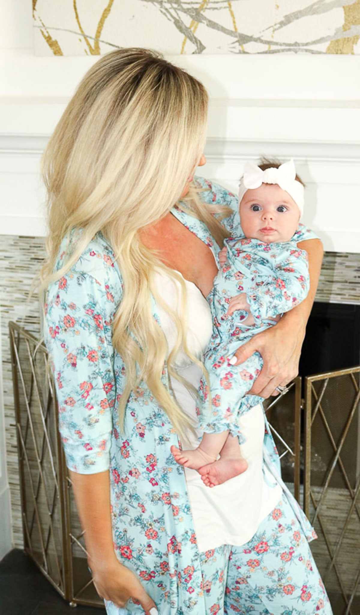 Azure Mist Baby's Ruffle Take-Me-Home set. Woman wearing Susan PJ in azure mist is holding baby girl wearing matching Ruffle Take-Me-Home top and pant with white hair bow.