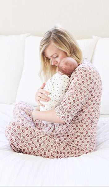 Pink Blush Susan 5-Piece. Image of woman wearing all-over printed robe and pant while sitting on a bed and holding swaddled baby.