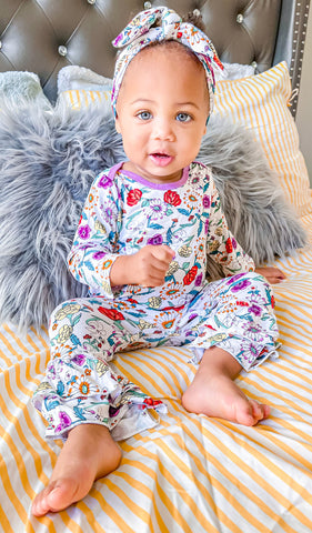 Zinnia Ruffle Romper 2-Piece on baby girl wearing matching headwrap while sitting in bed.