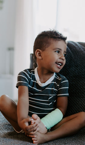 Charcoal Aydenne Kids 2-Piece Short PJ. Lifestyle shot of smiling boy sitting holding his feet wearing Aydenne.
