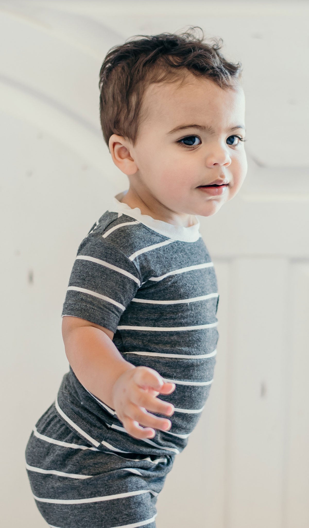 Charcoal Aydenne Baby 2-Piece Short PJ. Lifestyle shot of smiling boy standing wearing Aydenne.