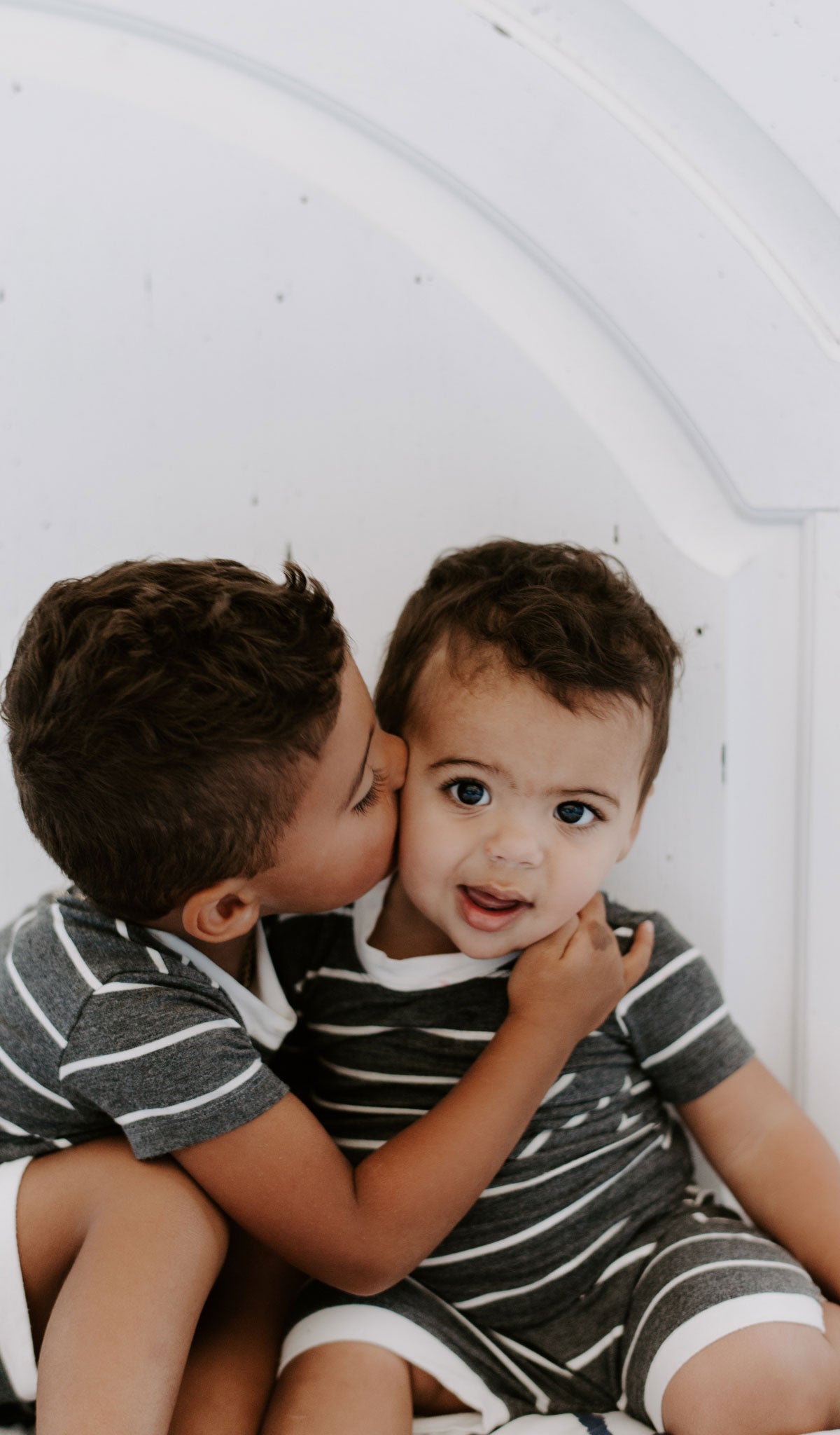 Charcoal Aydenne Baby 2-Piece Short PJ. Lifestyle shot of older boy hugging and kissing younger boy on the cheek, both wearing Aydenne.