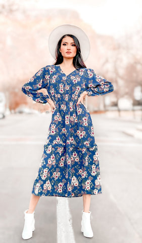 Blue Floral Jenny Dress. Lifestyle shot of woman standing with both hands on hips wearing Jenny dress as non-maternity with white rimmed hat and white booties.