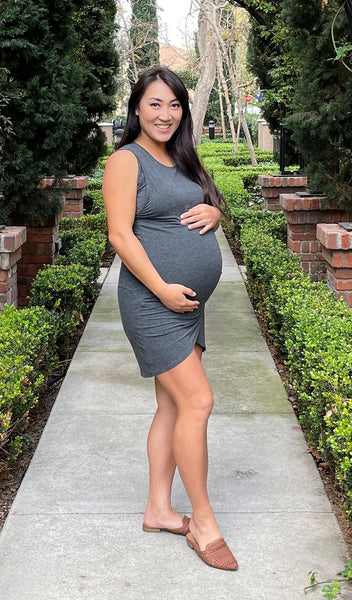 Charcoal Tamara dress worn by pregnant woman cradling her belly while standing in garden.