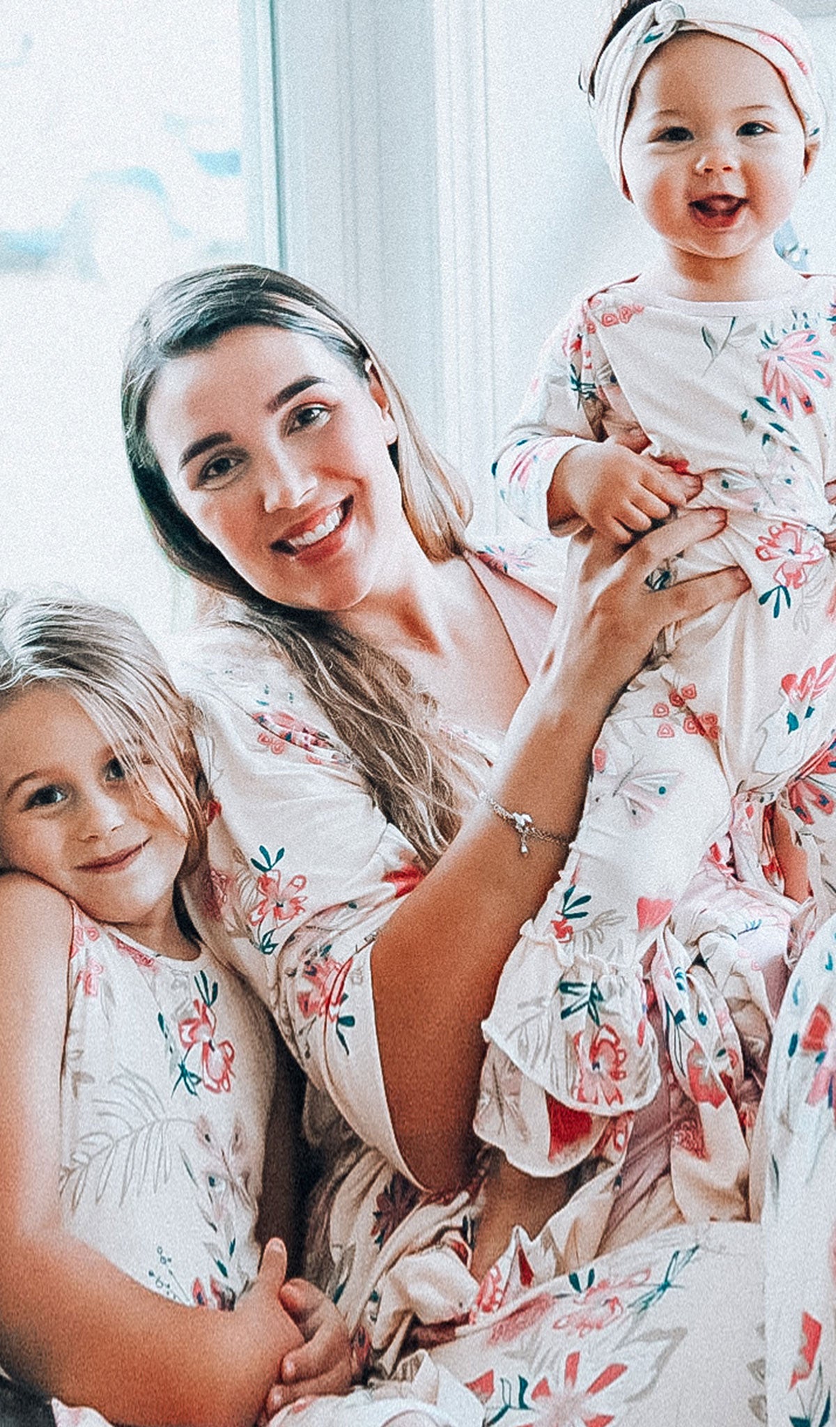 Wild Flower Ruffle Romper 2-Piece, woman wearing robe, tank top and pant from Wild Flower Analise PJ set while holding baby girl in matching Ruffle Romper 2-Piece set and sitting with girl in matching Lucia Twirly Dress.