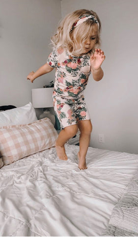 Beige Floral Bella Kids 3-Piece Short PJ. Little girl jumping on bed wearing short sleeve top and short with matching headwrap.