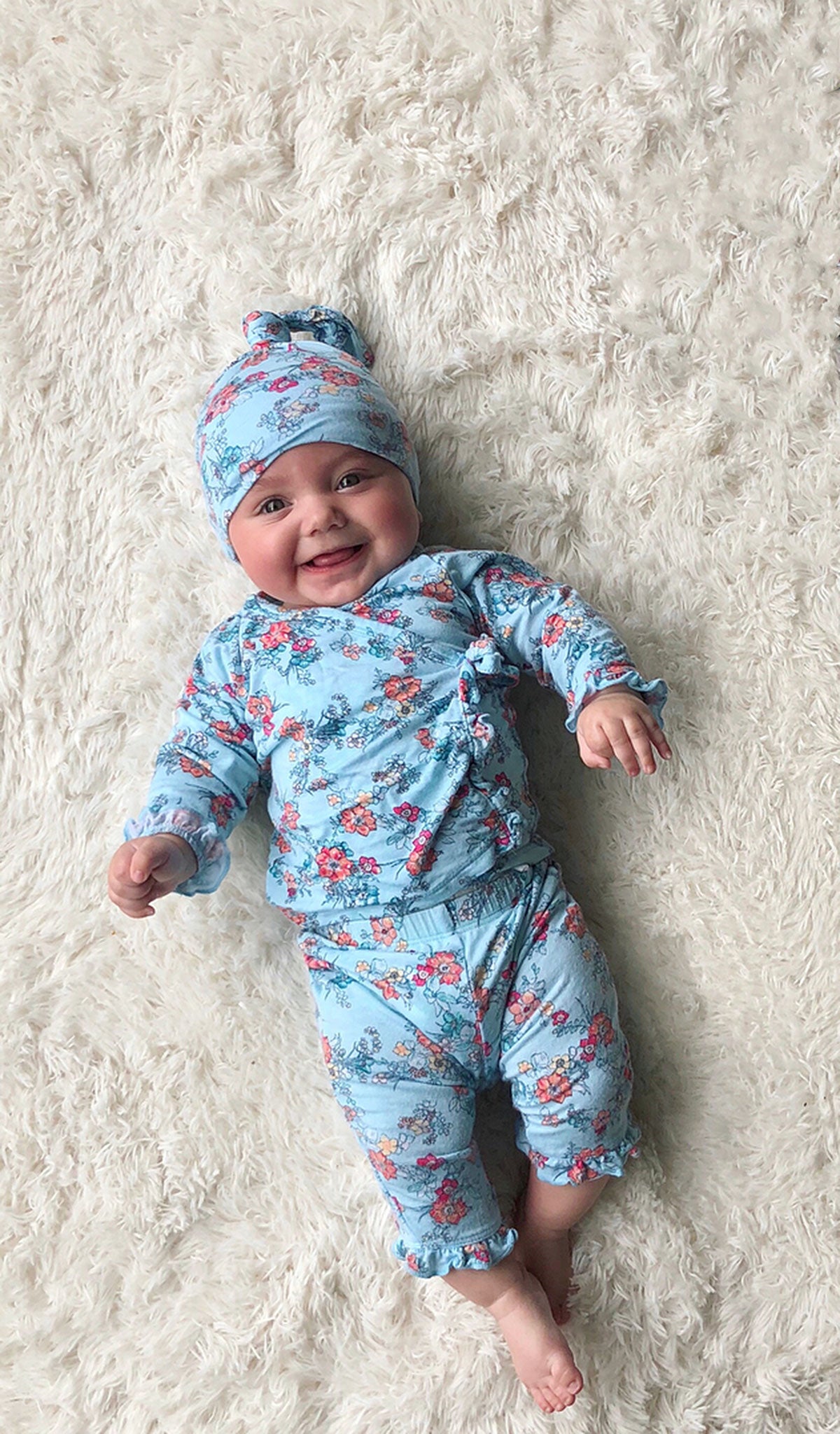 Azure Mist Baby's Ruffle Take-Me-Home 3 Piece set worn by baby girl laying on her back and smiling.
