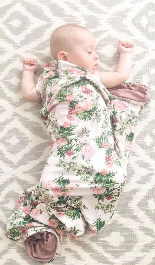 Beige Floral Swaddle Blanket, baby sleeping on back with arms up loosely swaddled in blanket.